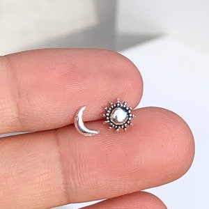 May include: A pair of silver earrings featuring a crescent moon and a sun with a textured surface.