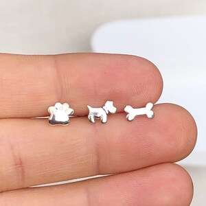 May include: Three silver earrings in the shape of a paw print, a dog, and a bone.