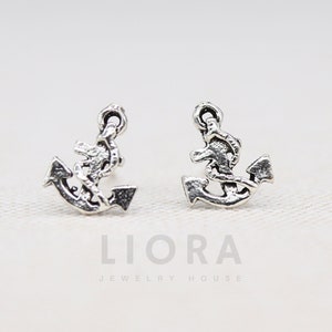 Könnte beinhalten: Ein Paar silberne Ankerohrringe. Die Anker sind mit einem Seil-Design verziert und haben einen einfachen Stiftverschluss.