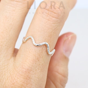 Puede incluir: Un anillo de plata con un diseño ondulado. El anillo es texturizado y tiene un acabado ligeramente martillado.