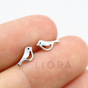 Może przedstawiać: Para srebrnych kolczyków w kształcie ptaka. Ptaki są zwrócone do siebie i mają prosty, minimalistyczny design.