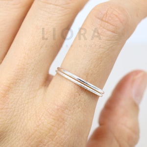 May include: Two thin silver rings stacked on a finger. The rings are simple and delicate.
