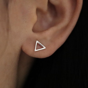 May include: A close-up of a person's ear with a small silver triangle stud earring.