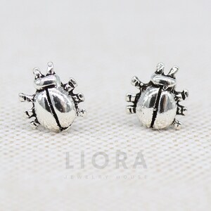 Peut inclure: Une paire de boucles d'oreilles clous en argent en forme de coccinelle. Les boucles d'oreilles sont petites et délicates, et elles présentent un design de coccinelle réaliste.