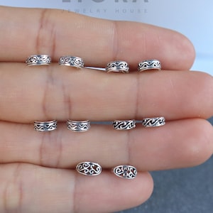 Puede incluir: Un conjunto de ocho anillos de nariz de plata con diseños intrincados. Los anillos están dispuestos en dos filas de cuatro, con la fila superior que presenta un diseño más ornamentado que la fila inferior.