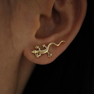 May include: Gold-toned lizard shaped ear crawler earring. The lizard is curled up with its tail extending out behind the ear.