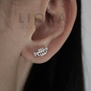 May include: Silver trumpet earrings. The earrings are small and delicate, and they feature a detailed trumpet design.