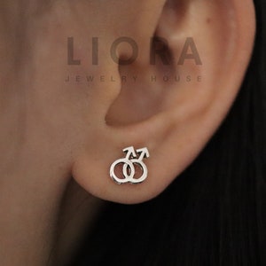 Pode incluir: Brincos de prata com um design estilizado de dois símbolos masculinos entrelaçados.