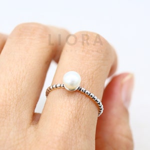 May include: A silver ring with a single white pearl in the centre. The ring is made of small beads.