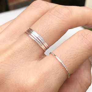 Puede incluir: Un conjunto de cuatro anillos finos de plata apilables en un dedo. Los anillos son lisos y tienen un acabado pulido.