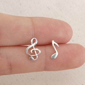 Puede incluir: Un par de pendientes de plata con una clave de sol y una nota musical. Los pendientes son pequeños y delicados, perfectos para añadir un toque de música a cualquier atuendo.