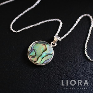 May include: A silver chain necklace with a round pendant featuring a green, blue, and iridescent abalone shell. The pendant is set in a silver bezel.