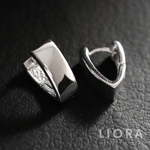 May include: A pair of silver-colored hoop earrings. The earrings have a geometric design with a flat, rectangular shape on the front and a curved back. The earrings are displayed on a dark surface.