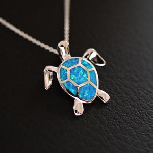 May include: A silver turtle pendant necklace with a blue opal inlay. The turtle is facing the right side of the image. The pendant is on a silver chain.