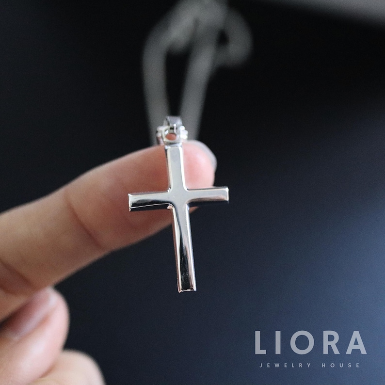 May include: A silver cross pendant necklace. The cross is simple and elegant, with a smooth, polished finish.