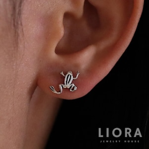 May include: A pair of silver frog stud earrings. The frog is facing to the right and has a detailed design.