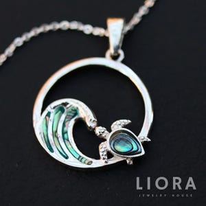 May include: A silver pendant necklace with a turtle and wave design. The turtle and wave have iridescent abalone shell inlays. The pendant hangs from a delicate silver chain. The jewelry is from Liora Jewelry House.