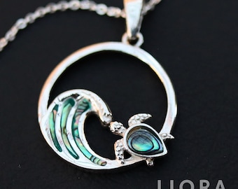 May include: A silver pendant necklace with a turtle and wave design. The turtle and wave have iridescent abalone shell inlays. The pendant hangs from a delicate silver chain. The jewelry is from Liora Jewelry House.