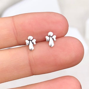 May include: A pair of silver angel stud earrings. The earrings are small and delicate, and they feature a simple design.