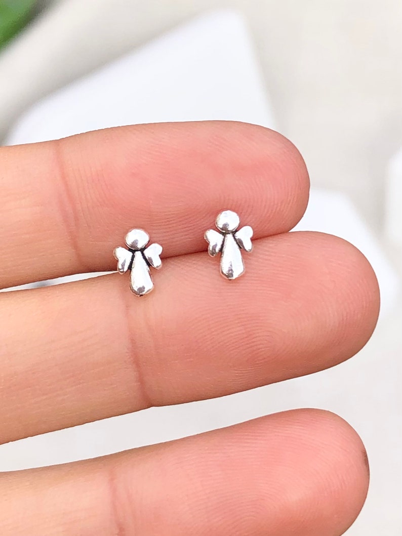 May include: A pair of silver angel stud earrings. The earrings are small and delicate, and they feature a simple design.