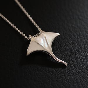 Puede incluir: Un collar de plata con un colgante de raya de nácar blanco.