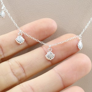 Puede incluir: Un collar de plata con una cadena delicada y cuatro pequeños colgantes de conchas marinas.
