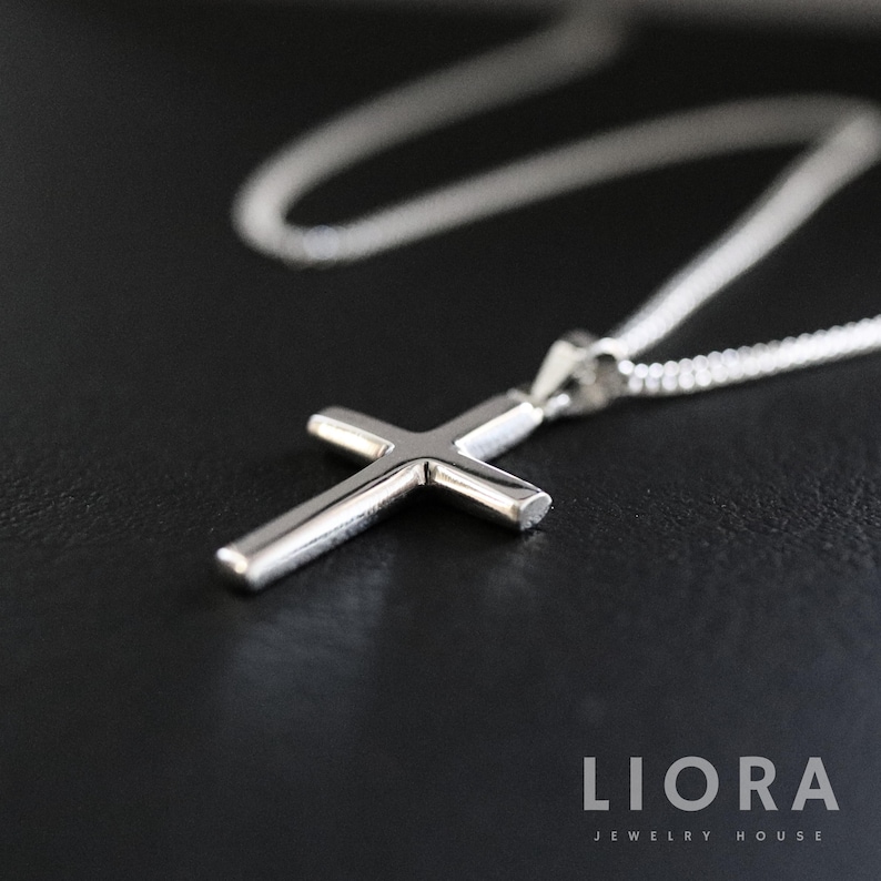 May include: A silver cross pendant necklace with a delicate chain. The cross is simple and elegant, with a polished finish.