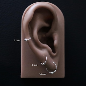 Op de afbeelding: Drie zilveren oorringen in verschillende maten, 6 mm, 8 mm en 10 mm, getoond op een oormodel.