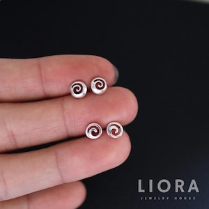 May include: A pair of silver spiral stud earrings. The earrings are small and delicate, with a simple design.