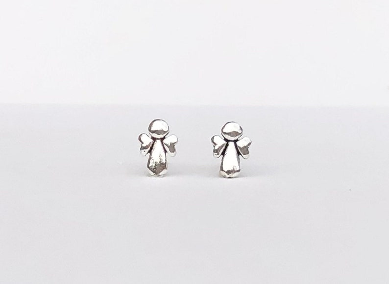 May include: A pair of silver angel stud earrings. The angels have small wings and a round head.