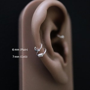 May include: Two silver ear rings, one is a plain hoop and the other is a coil hoop. The plain hoop is 6 mm and the coil hoop is 7 mm.