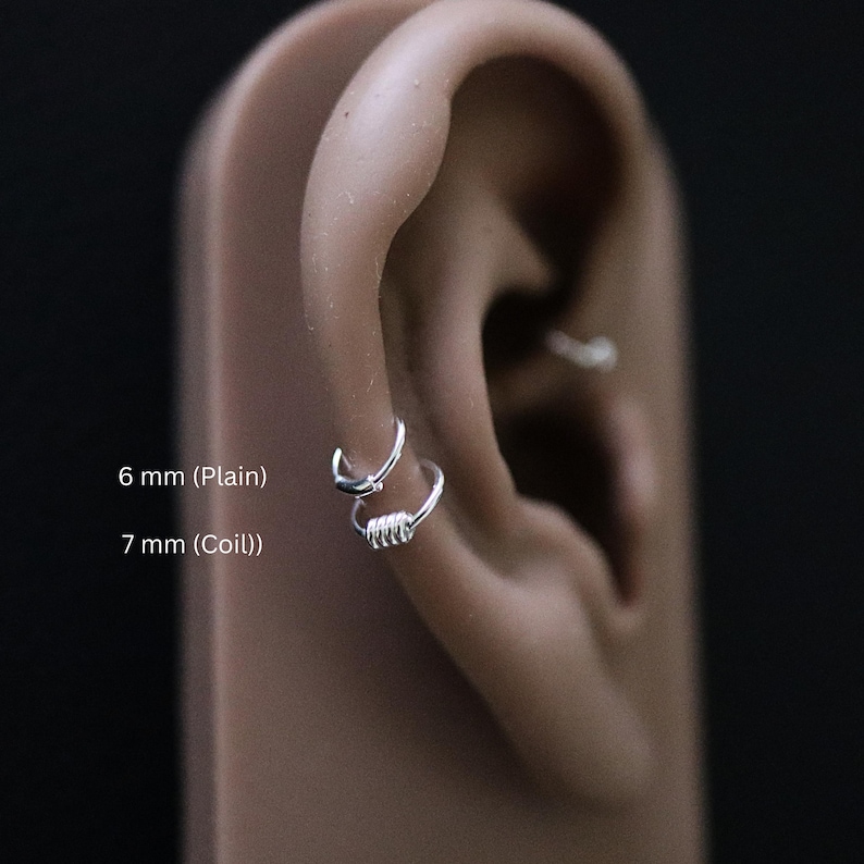 May include: Two silver ear rings, one is a plain hoop and the other is a coil hoop. The plain hoop is 6 mm and the coil hoop is 7 mm.