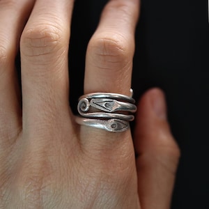 May include: A silver ring with a unique design featuring two diamond-shaped accents. The ring is made of multiple bands that are twisted and intertwined.