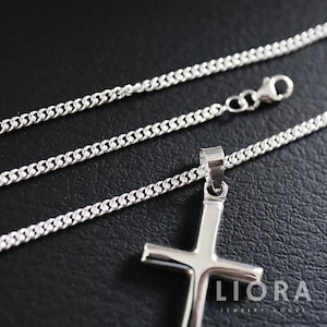May include: A silver chain necklace with a silver cross pendant. The chain is a curb chain style. The cross pendant is simple and has a smooth finish. The necklace is displayed on a black surface. Liora Jewelry House is printed on the surface.
