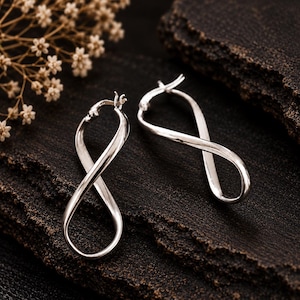 May include: A pair of polished silver hoop earrings featuring a twisted infinity loop design. Each earring has a hinged post closure at the top, creating a continuous, fluid shape that curves into a figure-eight silhouette.