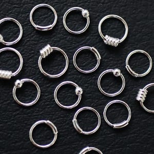 May include: A collection of silver hoop earrings with different embellishments, including a ball, a spiral, and a plain hoop.
