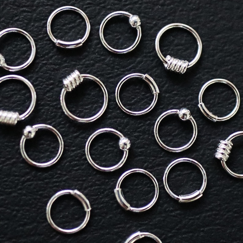 May include: A collection of silver hoop earrings with different embellishments, including a ball, a spiral, and a plain hoop.