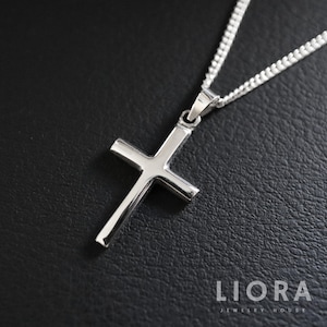 May include: A silver cross pendant necklace with a delicate chain. The cross is simple and elegant, with a smooth, polished finish.
