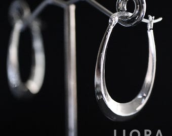 May include: Silver teardrop hoop earrings on a display stand. The earrings have a polished, reflective surface and a classic teardrop shape. The background is black, highlighting the jewelry. The brand name "LIORA JEWELRY HOUSE" is visible.