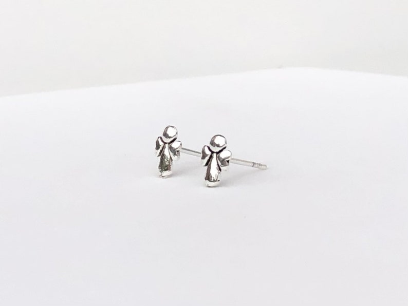 May include: A pair of silver angel stud earrings. The angel is depicted in a simple, minimalist style.