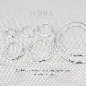 Puede incluir: Cinco pendientes de aro de plata de diferentes tama&ntilde;os. Los pendientes est&aacute;n dispuestos en una fila del m&aacute;s peque&ntilde;o al m&aacute;s grande. El pendiente m&aacute;s grande tiene un di&aacute;metro de aproximadamente 5 cm. El texto "LIORA JEWELRY HOUSE" es visible en la parte superior de la imagen.