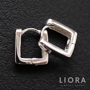 以下が含まれることがあります： シルバーの正方形フープピアス。ピアスは光沢のある反射性の金属でできており、シンプルでモダンなデザインです。黒い表面に表示されています。「LIORA JEWELRY HOUSE」のブランド名が右下に表示されています。