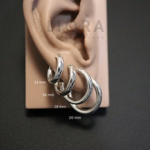 Peut inclure: Quatre créoles en argent de tailles différentes présentées sur un modèle d'oreille. Les anneaux sont étiquetés avec leurs diamètres respectifs de 14 mm, 16 mm, 18 mm et 20 mm. Le texte LIORA JEWELRY HOUSE est visible en haut du présentoir.