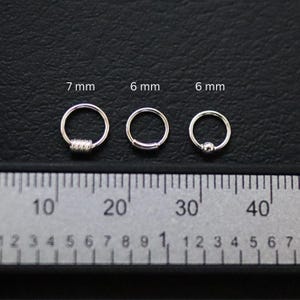 May include: Three silver hoop earrings of different sizes, measured in millimeters, displayed on a ruler. The earrings are 7 mm, 6 mm, and 6 mm in diameter.