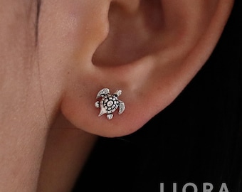 May include: Silver turtle stud earrings. The earrings are small and delicate, and the turtle is facing to the right.