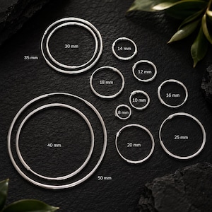 May include: A collection of silver hoop earrings in various sizes, labelled with diameters of 8 mm, 10 mm, 12 mm, 14 mm, 16 mm, 18 mm, 20 mm, 25 mm, 30 mm, 35 mm, 40 mm, and 50 mm. Each hoop is a simple, thin, circular wire design.