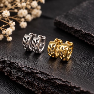 May include: Two pairs of small hoop earrings, one pair in silver-tone metal and one pair in gold-tone metal. Each hoop features a cut-out leaf or vine pattern along the outer surface, with a hinged closure mechanism visible on the side.