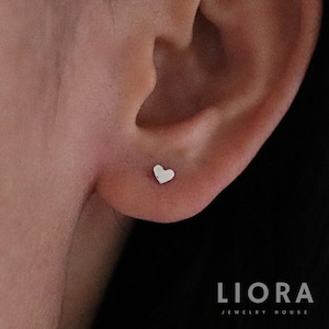 May include: A close-up of a person's ear with a small silver heart-shaped stud earring.