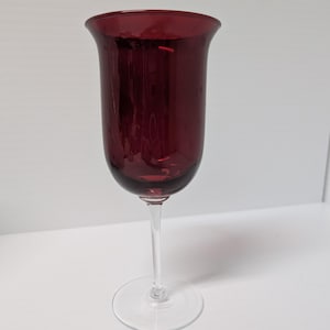 May include: A clear glass wine glass with a deep red coloured bowl. The glass has a long stem and a round base.