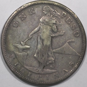 May include: A silver coin with the text "ONE PESO" and "FILIPINAS". The coin features a woman holding a hammer over an anvil, with a mountain in the background. The coin has a detailed edge.